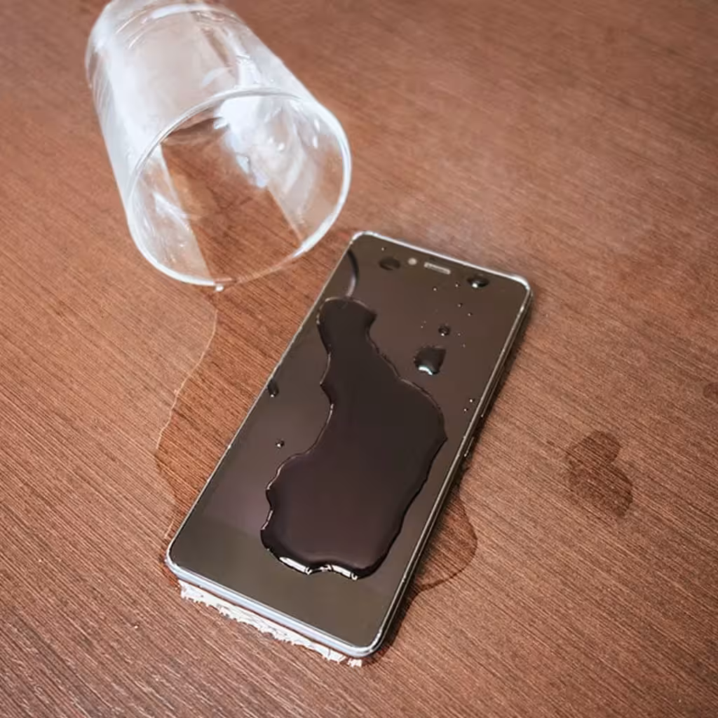 Smartphone lying face-up on a desk with water spilled across its screen